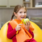girl smiling holding a tooth brush and apple